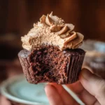 hand holding a gluten-free chocolate cupcake with a bite taken, showing moist crumb and whipped frosting